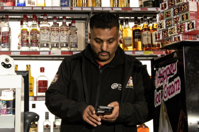 Search Never Sleeps shopkeeper on mobile phone behind alcohol counter news story