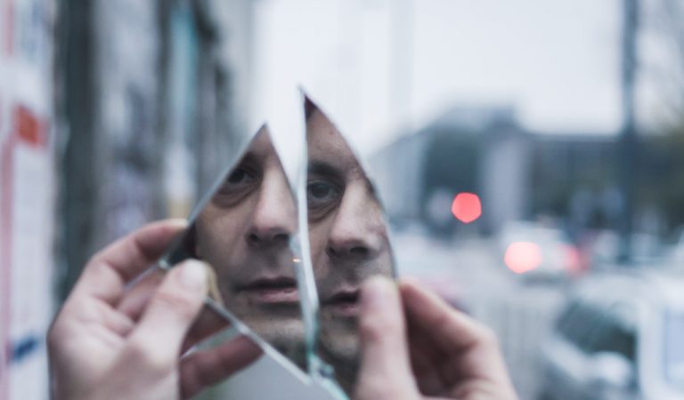 Man looking in two shards of glass at his face